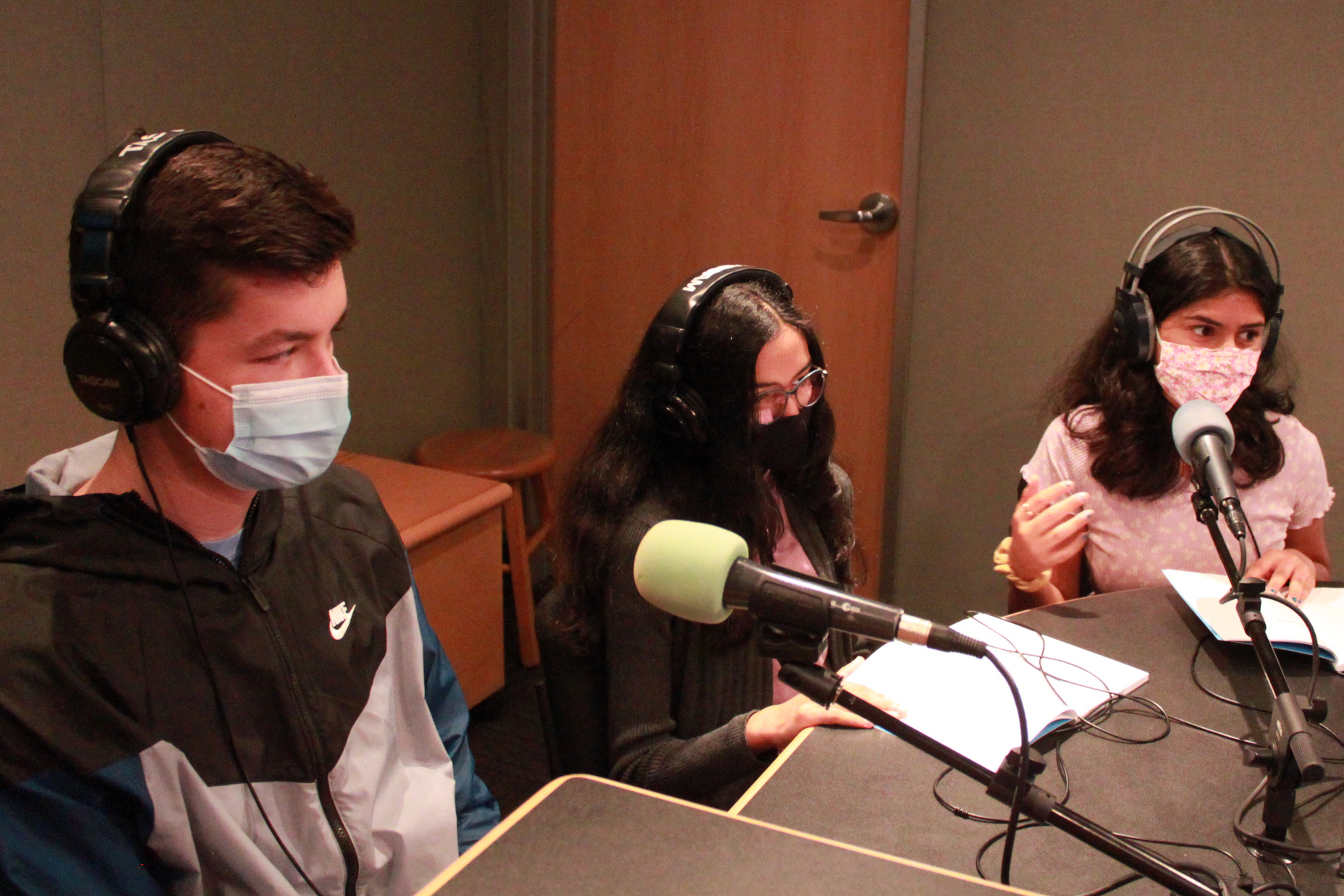 Three teens wearing face masks and headphones being interviewed in a radio studio