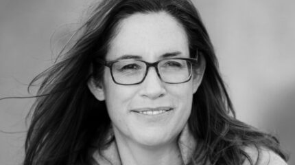 Black and white picture of adult with long hair and glasses smiling in profile