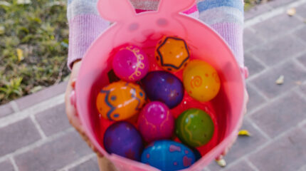 A person holding a pink bowl filled with multicolored plastic eggs