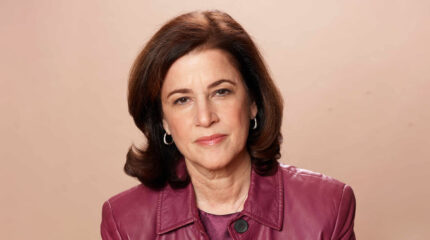 Adult with brown hair, earrings and a pink jacket posing in profile