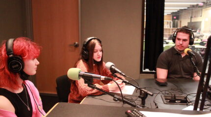 Three teens wearing headphones speaking into microphones in a radio studio