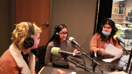Three youth wearing headphones speaking into microphones being interviewed in a radio studio