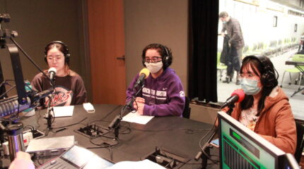 Three teens wearing headphones in front of microphones in a radio studio