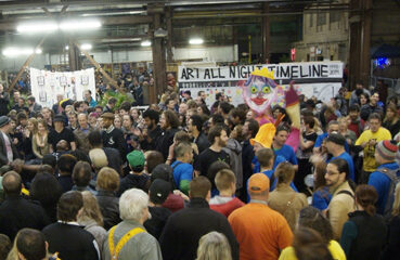 A crowd of people in front of a banner reading "Art All Night Timeline"