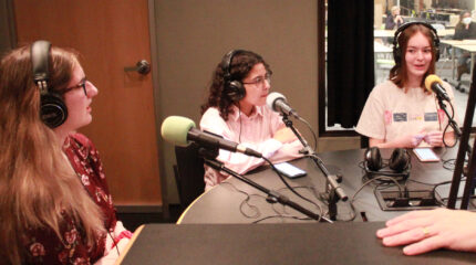 Three teens wearing headphones being interviewed in a radio studio