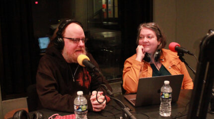 Two adults wearing headphones being interviewed in a radio studio