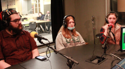 Three youth wearing headphones being interviewed in a radio studio