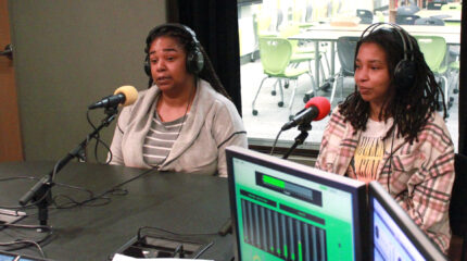 Two people wearing headphones being interviewed in a radio studio