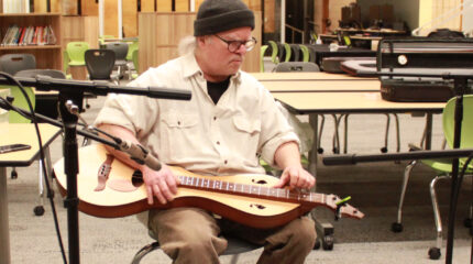 An adult in a black beanie performing on a lap dulcimer