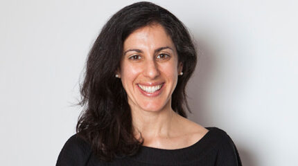 Adult with long dark brown hair, earrings, and a black top smiling in profile