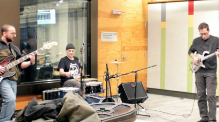 Three adult musicians performing on guitar, bass, and drums