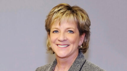 Adult with brown hair and blond highlights, earrings, and gray eyes smiling in profile