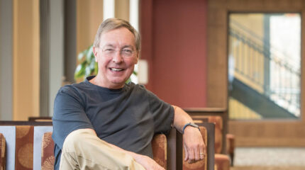 Adult with short gray hair, glasses, and a gray shirt smiling in profile