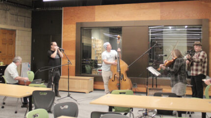 Five adults performing on a dobro, a harmonica, an upright bass, a guitar, and a violin
