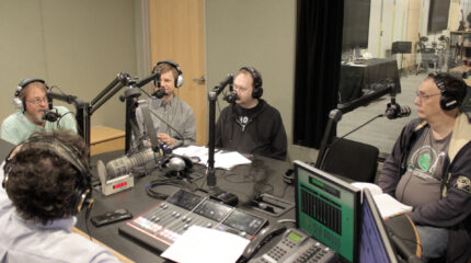 Four adults wearing headphones being interviewed in a radio studio