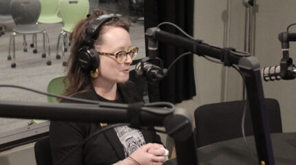 adult with glasses speaking into a microphone in a radio studio