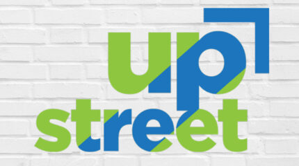 The text "UpStreet" written in blue and lime green on a white painted brick wall