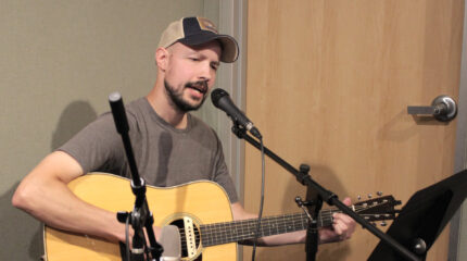 Adult playing guitar and singing into a microphone in a radio studio