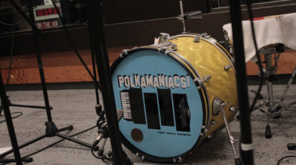 A bass drum with a graphic of a black accordion and the text "Polkamaniacs!" in white with black shadows, all on a blue background
