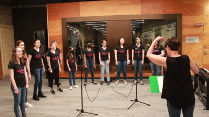 Eleven youth singing in a choir with an adult conducting them