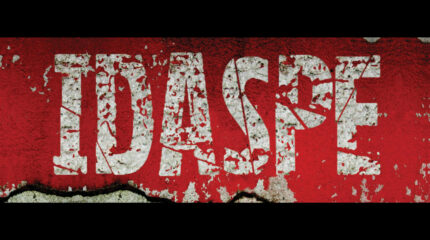The letters "IDASPE" in faded white paint on a red peeling background
