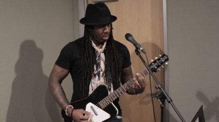 Adult playing a guitar standing behind a microphone in a radio studio