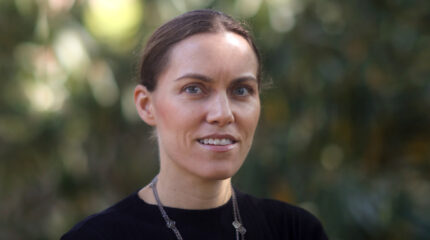 Adult with brown hair and a black top smiling in profile