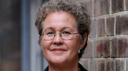 Adult with short gray hair, glasses, and earrings posing in profile