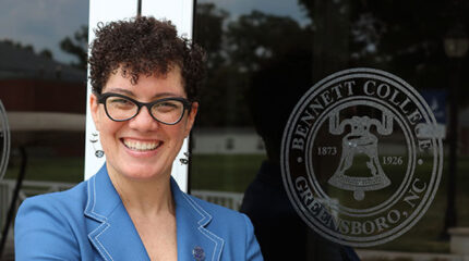 Adult with short brown hair, glasses, and a blue blazer smiling in profile