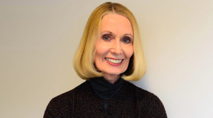 Adult with a blond bob haircut, blue eyes, and a black top smiling in profile