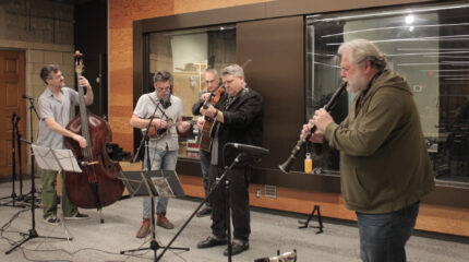 An adult playing upright bass, an adult playing mandolin, an adult playing violin, an adult playing guitar, and an adult playing clarinet