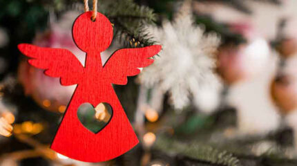A red wooden angel hanging from a Christmas tree