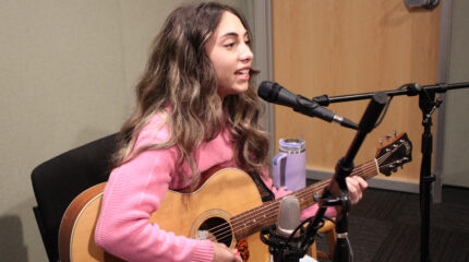 A teen playing acoustic guitar and singing into a microphone in a radio studio