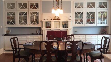 A brown dining room table and six brown chairs in a white room with a large number of cabinets and drawers