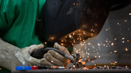 An individual in a blast mask holding a welding tool sparking metal