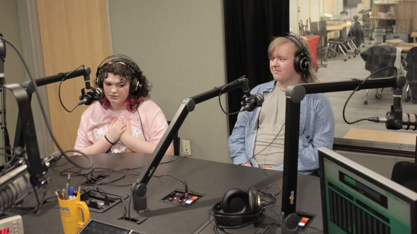 Two teens wearing headphones speaking into microphones being interviewed in a radio studio