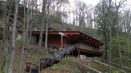 A brown house built into the side of a rocky hill with a long dark brown staircase