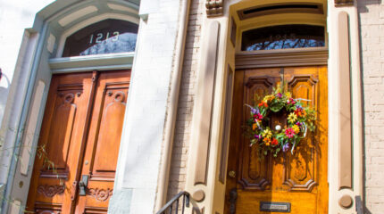 Two wooden front doors surrounded by pink bricks, one door with a wreath