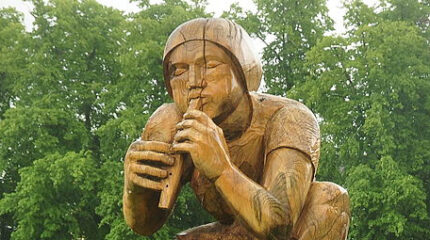 A wooden statue of an individual playing a whistle in a forest