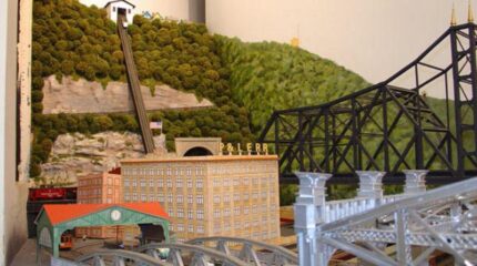 A model mockup of a trolley on a large wooded hill in front of bridges