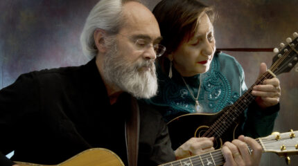An adult playing acoustic guitar and an adult playing mandolin