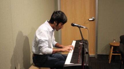 A teen playing a piano keyboard sitting behind a microphone in a radio studio