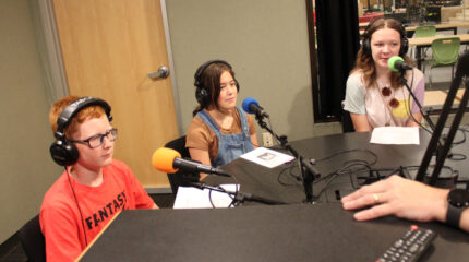 Three youth wearing headphones speaking into microphones being interviewed in a radio studio