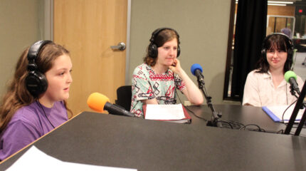 Three teens wearing headphones speaking into microphones in a radio studio