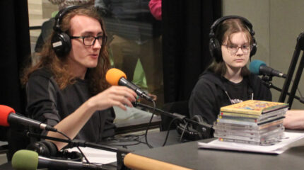 Two teens wearing headphones speaking into microphones in a radio studio
