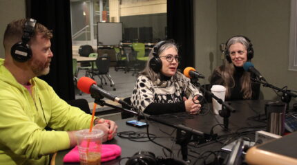 Three adults wearing headphones speaking into microphones in a radio studio