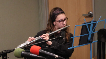 A teen playing flute while looking at an ipad on a music stand in a radio studio