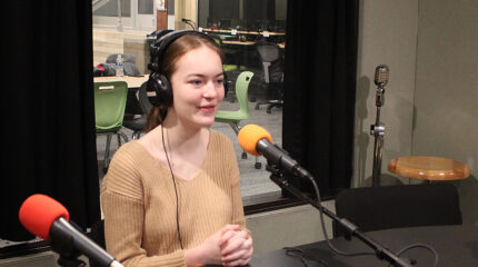 A teen wearing headphones speaking into a microphone in a radio studio