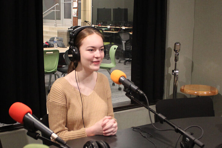 A teen wearing headphones speaking into a microphone in a radio studio