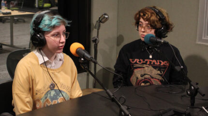 Two teens wearing headphones speaking into microphones in a radio studio